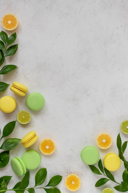 Colorful macarons with green branches, slices of lemon, lime white surface