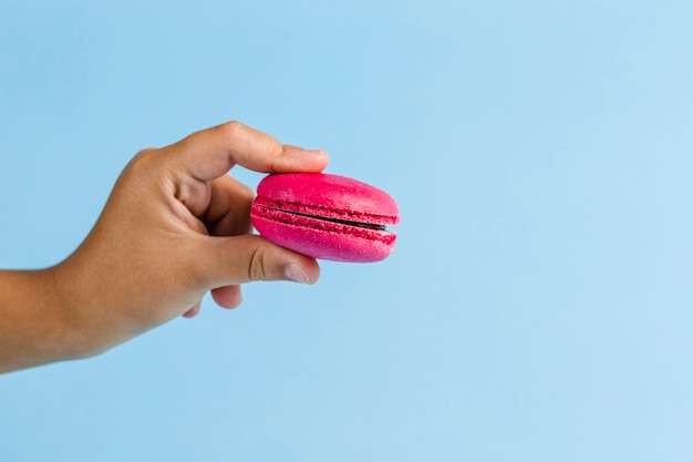 Colorful macaroons in a child's hand on a blue copyspace, close-up, Flatley with copyspace