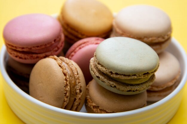 Colorful macaroons cookies dessert on a plate, with yellow table.