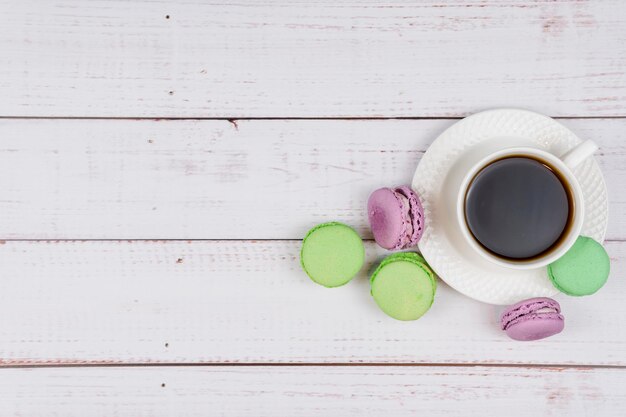 Colorful macaroons and a cup of coffee on wooden background closeup flat lay