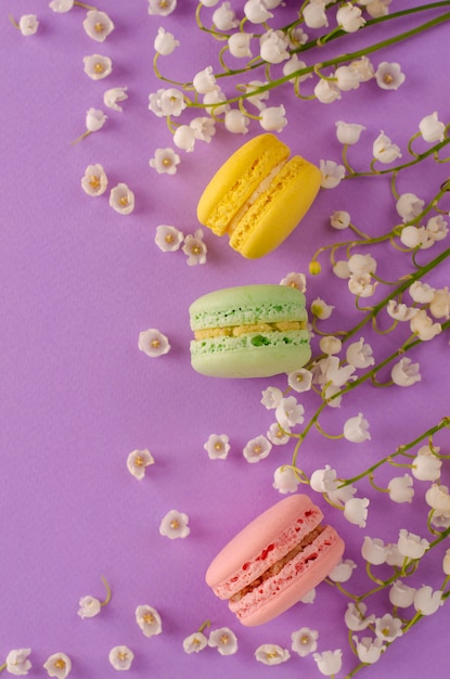 Colorful macaroons decorated with blooming lily of the valley on purple. Sweet french dessert concept. Frame composition. Flat lay. copyspace. Vertical. Greeting card concept