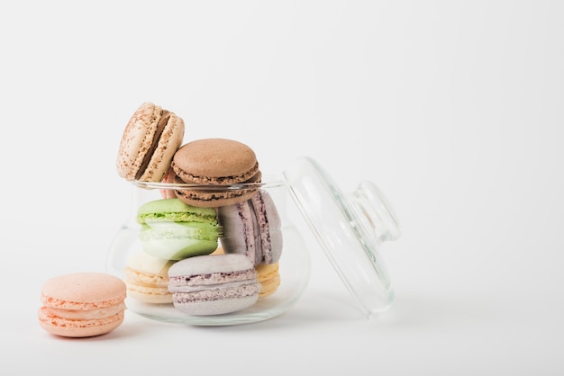 Colorful macaroons in transparent open glass jar on white backdrop