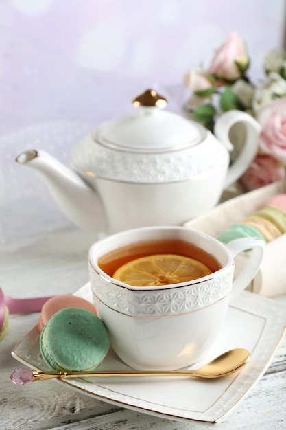 Colorful macaroons with cup of tea on color wooden table on light background