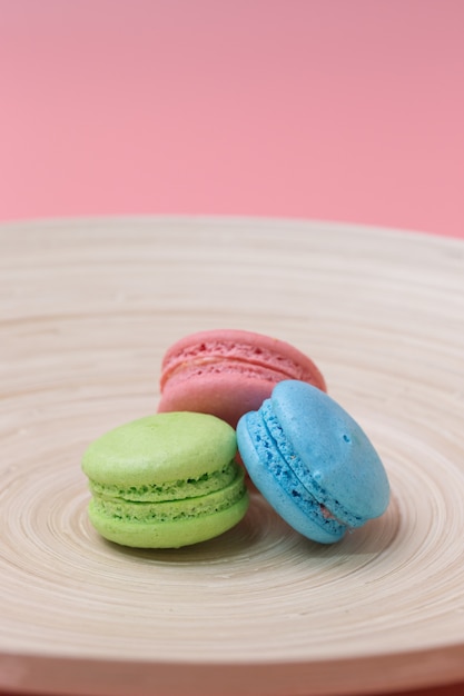 colorful macaroons in wood plate on pink background.