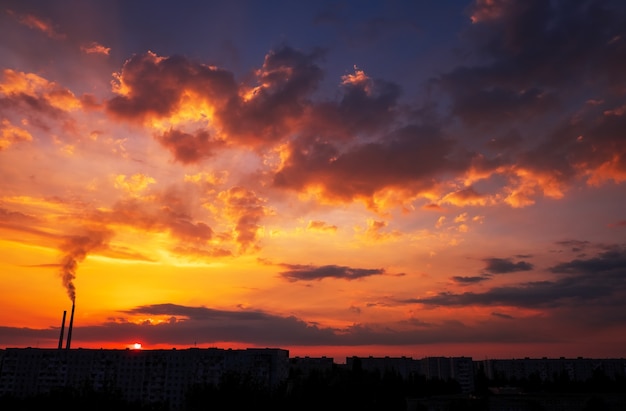 Colorful Magic Sunset. Roofs of city houses during sunrise. Birds flying in the sky. Dark smoke coming from the thermal power plant pipe.