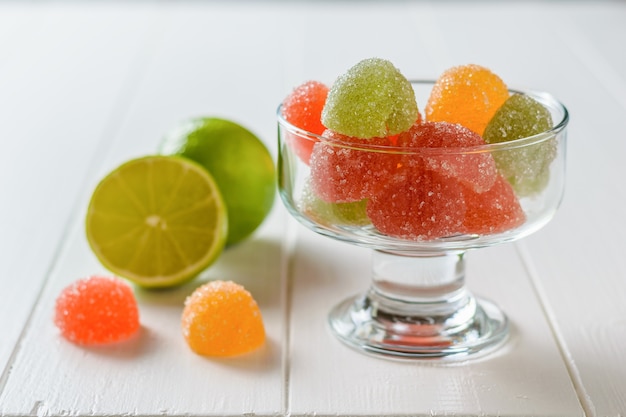 Colorful marmalade in a glass bowl and lime on a white rustic wooden table. Delicious sweets made of jelly with sugar.