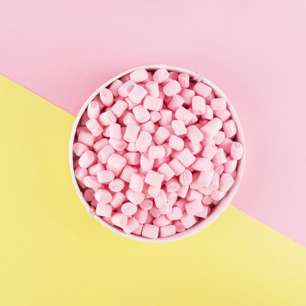 Marshmallow colorato steso sulla superficie della carta rosa e gialla