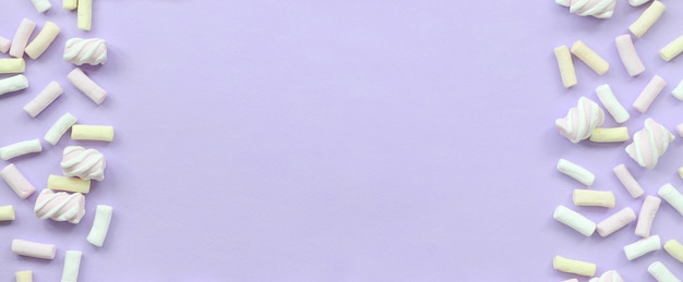 カラフルなマシュマロは紫色の紙の背景にレイアウトしました。パステルカラーのクリエイティブテクスチャフレームワーク。最小限の