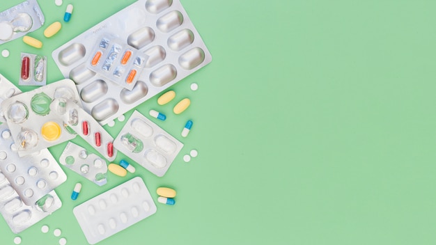 Colorful medical pills and sliver blister packs on green background