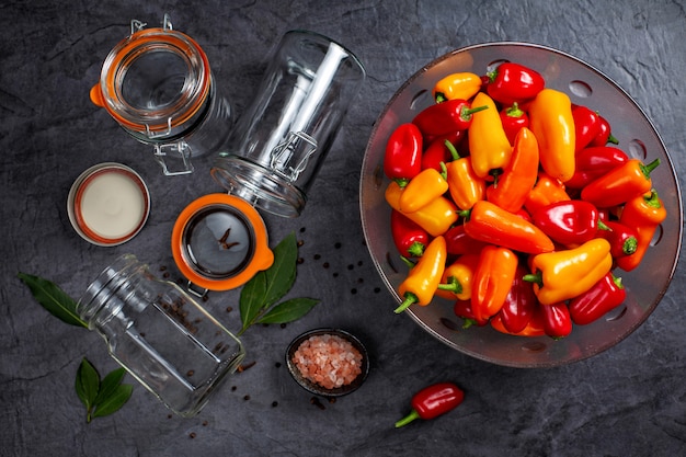 colorful  mini bell peppers in glass bowl  and empty glass jars ready to be marinated on dark surface, top view