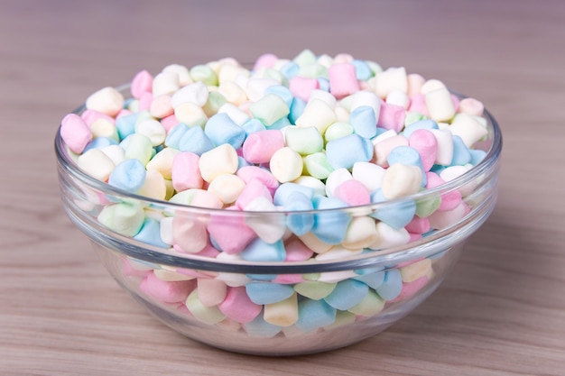 Colorful mini marshmallows in glass bowl on wooden table