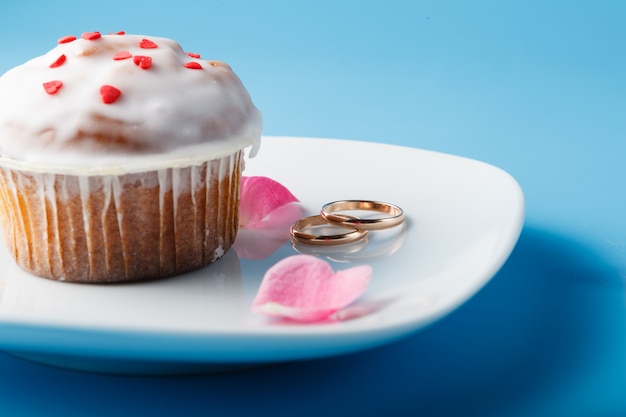 Colorful muffin on saucer with wedding rings