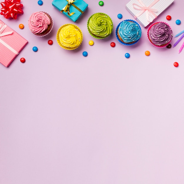 Photo colorful muffins and gems with wrapped gift boxes on pink backdrop