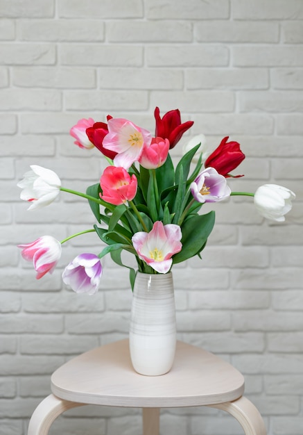 Colorful multi-colored tulips in a vase in a modern interior against a white brick wall.