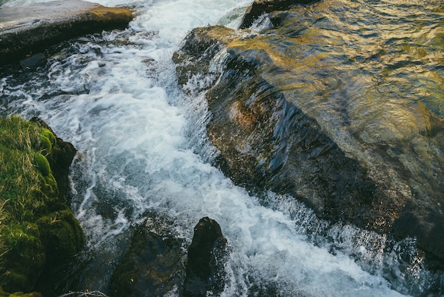 Colorful nature background with big boulder in turbulence of mountain river in sunny day. Beautiful landscape with moss near mountain river. Big stone in water stream in sunshine. Mossy water edge.