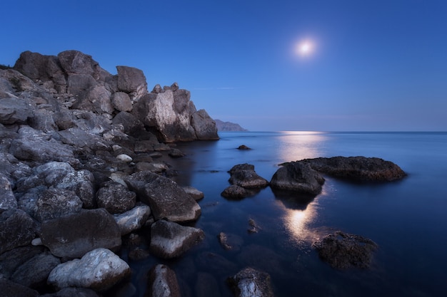 Paesaggio notturno colorato con luna piena, percorso lunare e rocce in estate