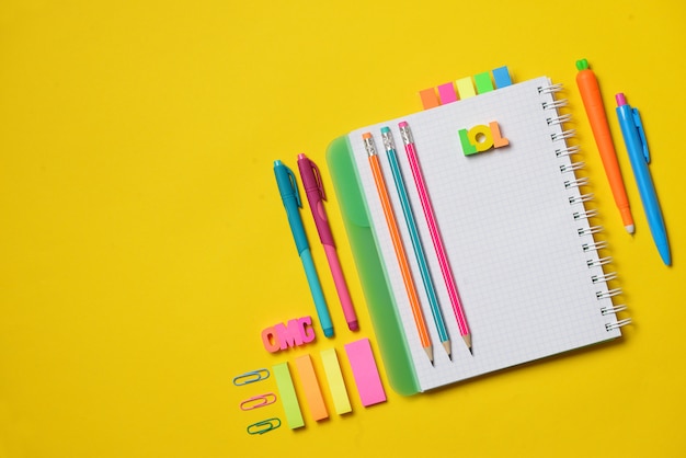 Foto libro aperto variopinto della copia con i rifornimenti dello studente e dell'ufficio su gesso giallo. spazio per il testo.