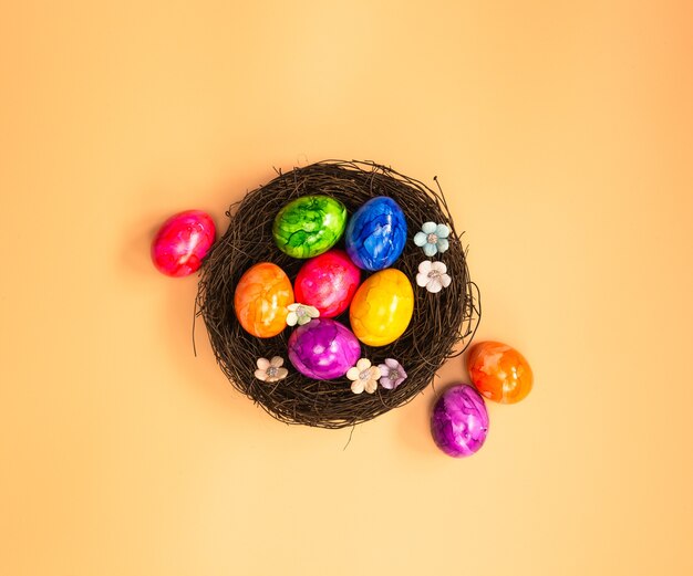 Colorful painted Easter Egg Nest with orange pastel colored background top view, Happy Easter Holliday concept background