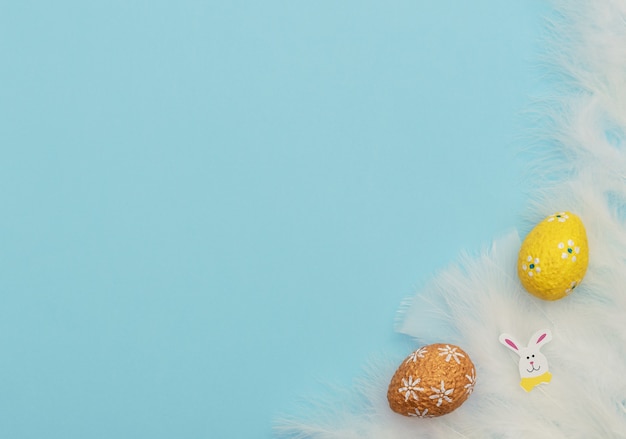 Colorful painted orange and yellow Easter eggs with Easter rabbit and white feathers on blue