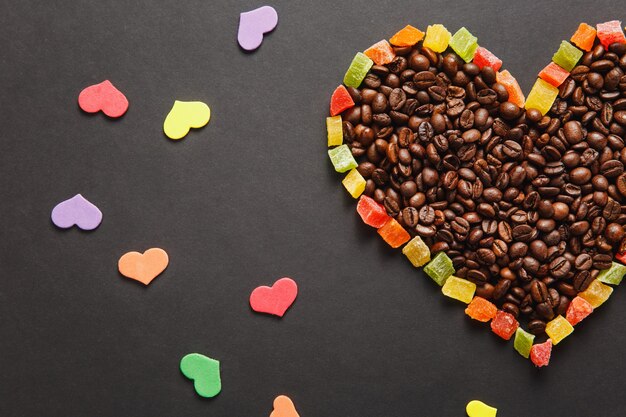 Colorful paper, candied fruits in the form of heart, brown coffee beans isolated on black background for design. Saint Valentine's Day card, fabruary 14, holiday concept. Copy space for advertisement.