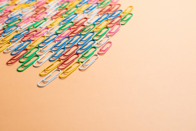 Photo colorful paper clips on orange background. back to school. various color wire plugs are one type of office material. copyspace