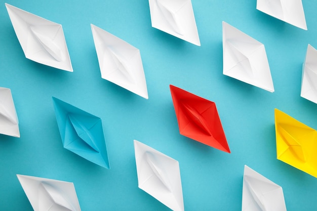 Colorful paper ships on blue background Leadership and Business competition concepts
