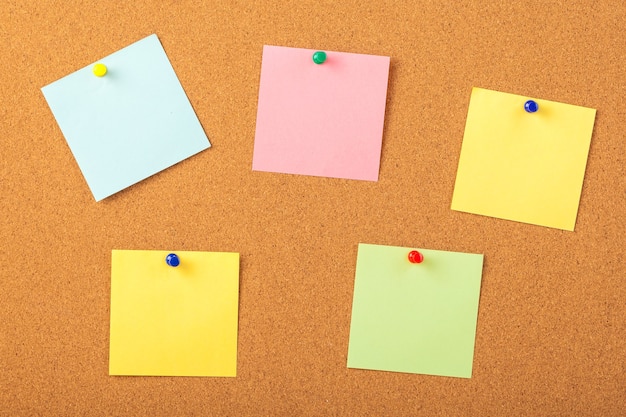 Colorful papers pined with tacks on brown cork board background.