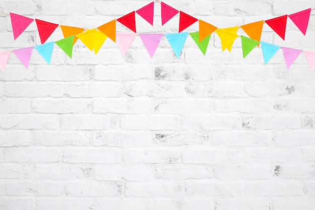 Colorful party flags hanging on white brick wall background