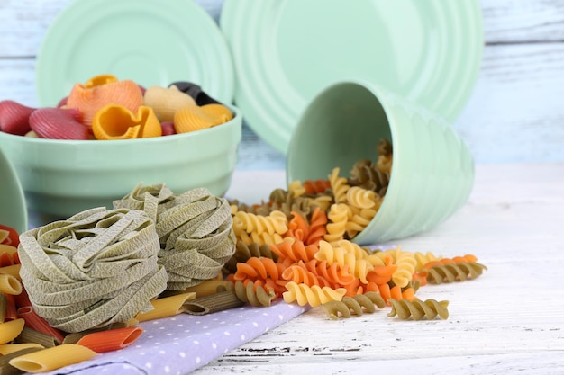 Colorful pasta in color bowls and mugs on wooden background