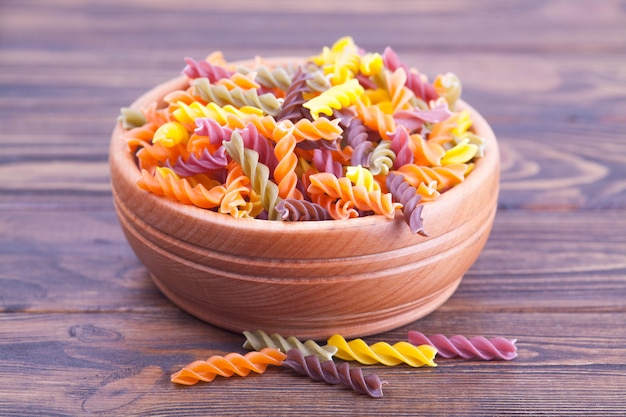 Colorful pasta fusilli with spinach, carrots, beets in a wooden bowl on a dark table