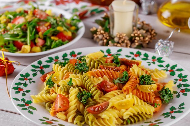 Colorful pasta rotini, cherry tomatoes on christmas table with salad