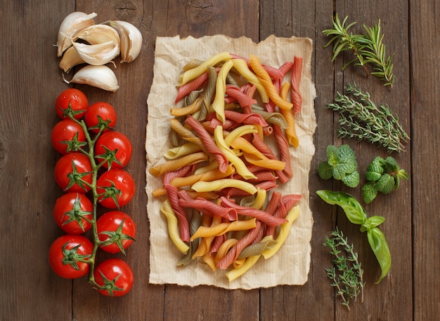 Colorful pasta, vegetables and herbs on a wooden table  top view