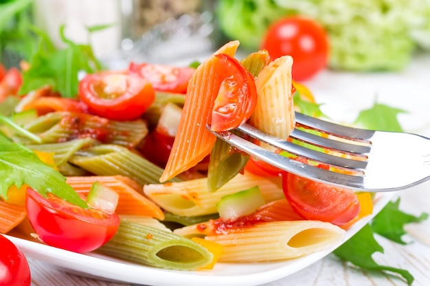 Colorful pasta with vegetables on a white plate on a wooden