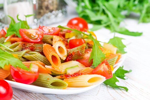 木製の白いプレートに野菜とカラフルなパスタ