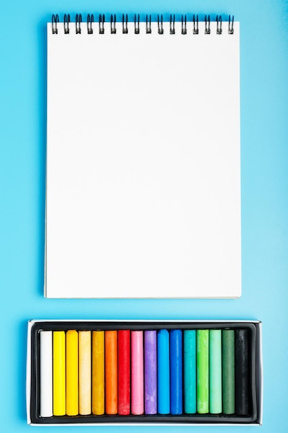 Foto quaderno bianco pastello colorato e bianco su sfondo blu concetto di corso di disegno per bambini e adulti mockup di spazio piatto per la copia