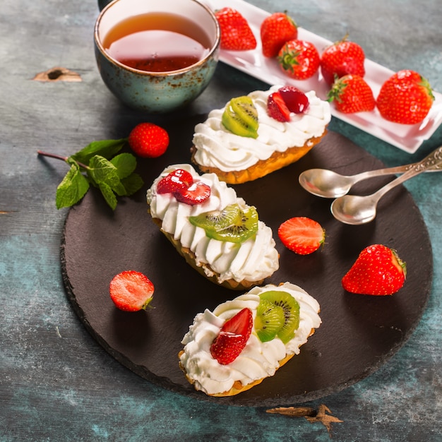 Colorful pastry cakes with chantilly cream, fruits and berries on grunge blue wooden background