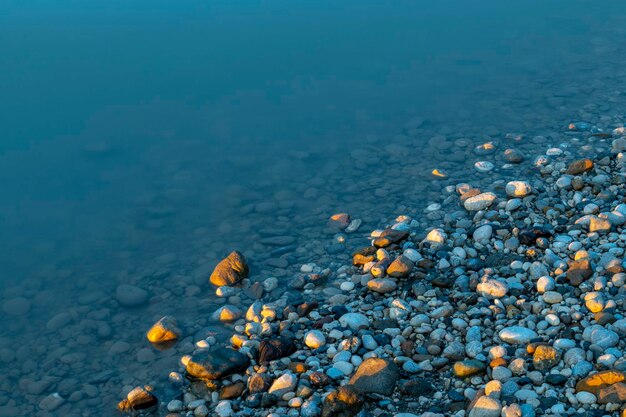 Colorful pebbles on the blue river shore photographed at the last minutes of golden sunset