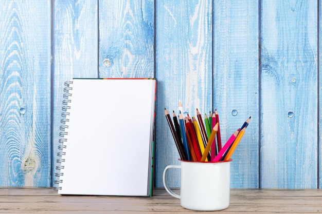 Colorful pencils in a cup and blank notepad