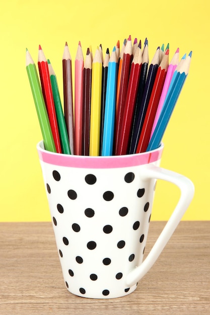 Colorful pencils in cup on table on yellow background