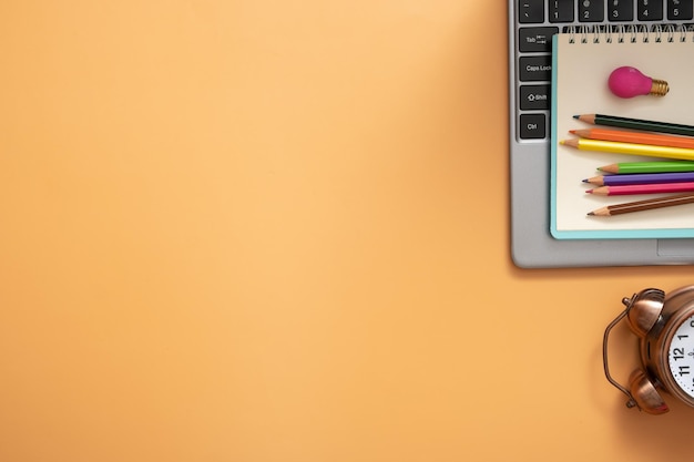 Colorful pencils and note on laptop with alarm clock on colored background Copy space Top view flat lay