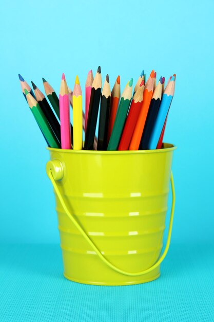 Colorful pencils in pail on blue background