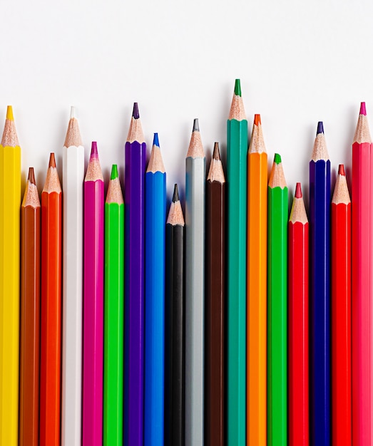 Colorful pencils on white wall. Flat lay, copy space