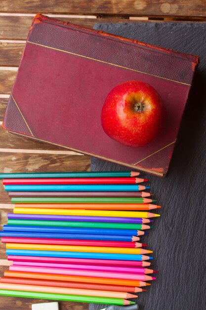 Colorful pencils with old book and red apple on black board