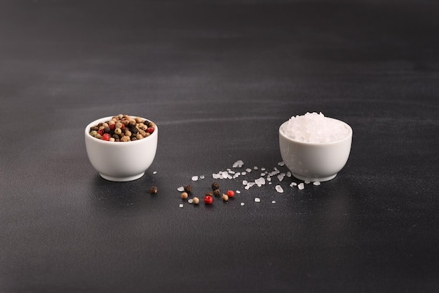 Colorful pepper and salt in small white small bowls on a dark background