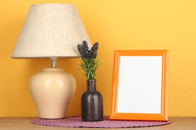 Colorful photo frame lamp and flowers on wooden table on yellow background