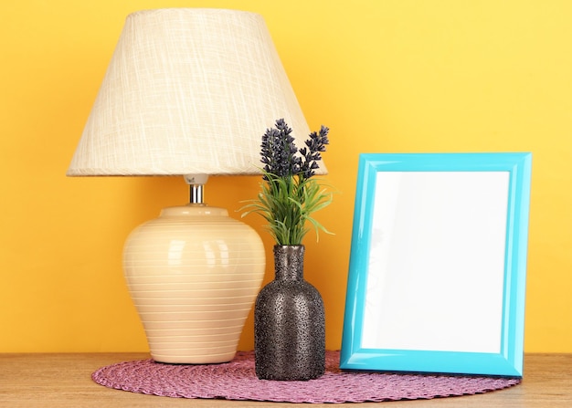 Colorful photo frame lamp and flowers on wooden table on yellow background