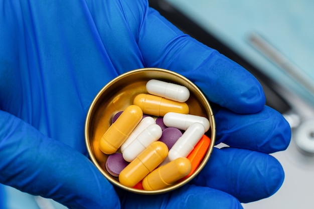 Colorful pill, tablet in hand in a blue medical glove isolated. antiviral protection, treatment of viruses, diseases concept.