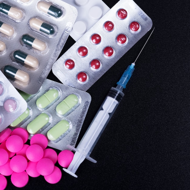 Colorful pills, blister and syringe on a black background.