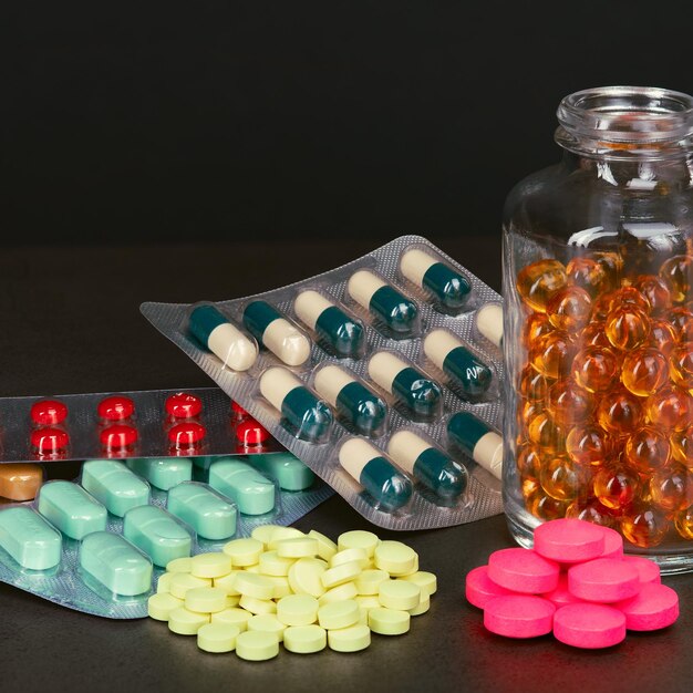 Colorful pills, blister and syringe on a black background.