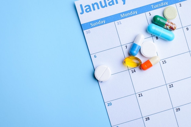 Photo colorful pills and capsules on calendar on light blue background